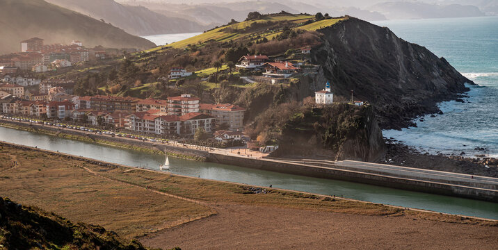View of Zumaia and its lighthouse. A sailing boat sails down the Urola River towards the sea.
