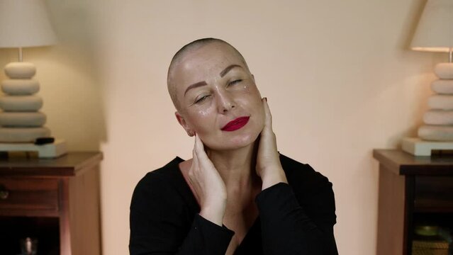 Portrait of happy woman is touching her hairless head and gets tactile pleasure. Close-up of a satisfied bald caucasian woman with red lipstick.