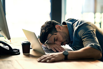 Defeated by the deadline. Shot of an exhausted young businessman sleeping at his desk during a late...