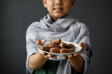 Cropped smilling muslim boy hand holding plate of dates on blurred background