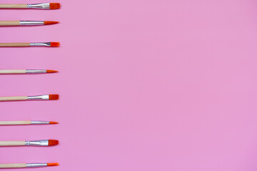 set of paint brushes on a pink background, top view, flat lay, space for text  