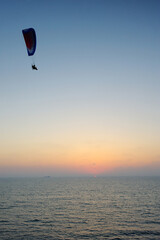 Powered paraglider flying over the sea at sunset sky background