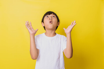 Little boy with shocked expression looking up while opening his palms isolated on yellow background