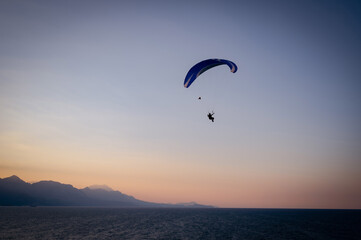Silhouette of a man on a paraglider flying over the sea at sunset.