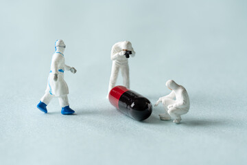 Miniature doctors doing research on pills. Concept for covid-19 medications.