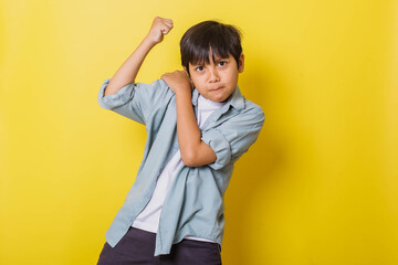 Angry boy showing his power by raising fist to challenge isolated on yellow background