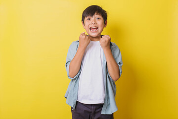 Happy little boy clenching fist for celebrating success isolated on yellow background