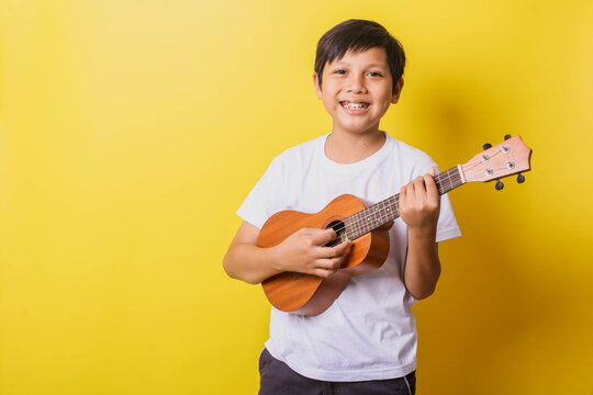 Happy little boy playing ukulele isolated on yellow background