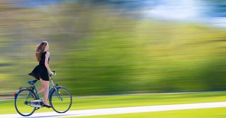 Fototapeta na wymiar a young woman in a short dress very quickly rides a bicycle in the park blurred background