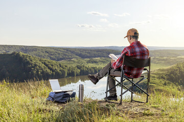 Man traveler reading book outdoor in mountains at sunset. Remote work concept. Hiking active people lifestyle.