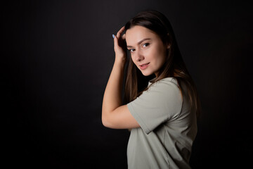 Young beautiful brunette, calm portrait on a black background. A positive and friendly young woman in a T-shirt