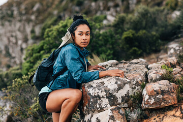 Portrait of woman hiker climbing a rock and looking away. Female with backpack hiking over terrain in a mountain.
