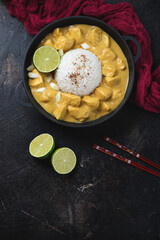 Yellow chicken curry and white rice in a cast-iron pan, vertical shot on a dark-brown stone surface, top view, copy space