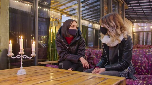 two happy women spend time together in a cafe, restaurant, wearing protective masks. quarantine period. romantic evening by candlelight, light atmosphere, lifestyle. drinking coffee together.