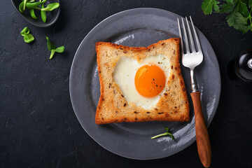 Breakfast on Valentines Day. Fried eggs and bread in the shape of a heart and fresh vegetables on black background. Breakfast with surprise for loved ones.  Top view. Mock up.