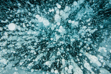 Texture of beautiful blue ice with cracks and air bubbles in the frozen lake. Winter nature background.