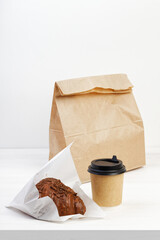 Chocolate covered croissant and cardboard cup of coffee on white wooden table. Copyspace.