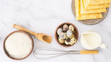 Ingredients for making pancakes and ready-made pancakes on a plate