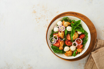 Panzanella Bread Salad. Traditional food of Italy with tomatoes, mozzarella balls, basil, onion and bread on plate on light background. Traditional Italian cooking. Top view. Copy space.