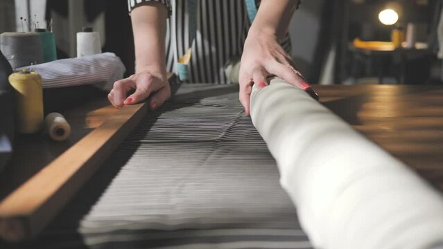 female tailor hand unrolling fabric in workshop slow motion,stylish dressmaker woman unroll textile material on work table close up dolly shot at the workplace
