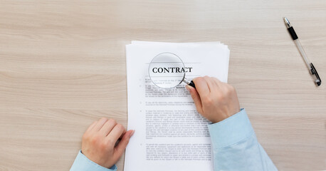 Fototapeta na wymiar contract study. Business and marketing. Women's hands hold a magnifying glass and study the contract. The document lies and the pen lie on a wooden table. The concept of studying a contract before sig