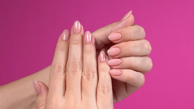 Closeup top view full hd video footage of elegant pastel pink natural manicure. Female hands isolated on pink bright color texture background. Pink professionally manicured nails of european woman