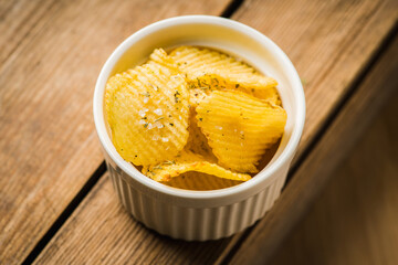 Salty grooved chips in white ceramic bowl on the rustic background. Selective focus. Shallow depth of field.