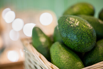 Organic farm avocado in straw basket on wooden table closeup. Fresh ripe green exotic fruits
