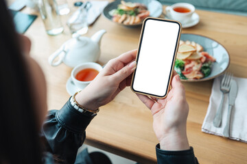 The girl holds a phone in her hands with a blank isolated screen on the background of food in a restaurant. Place for your menu or review.