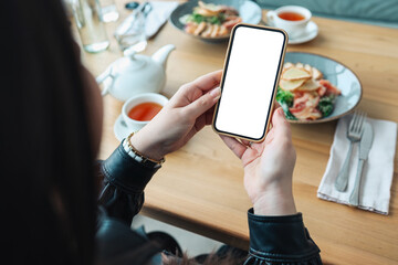 The girl holds a phone in her hands with a blank isolated screen on the background of food in a restaurant. Place for your menu or review.