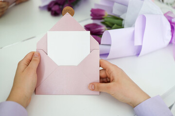 Woman's hands hold an empty white card on the background of a bouquet of tulips. Holiday greeting concept. Place for your text
