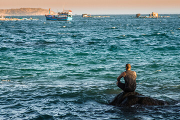 a lonely man sits on the seashore and looks into the distance at the ship