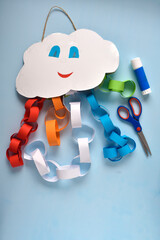 cheerful cloud made of cardboard and colored paper, scissors, glue on a blue background