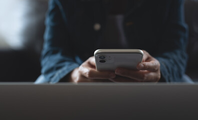 Close up on casual business woman hands holding, using mobile smart phone and online working on laptop computer at home office