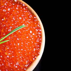 Red caviar in a white cup on a black background.