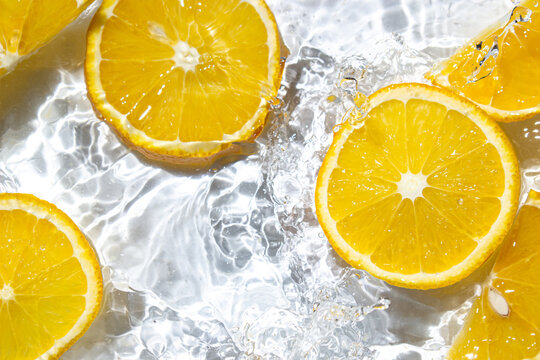 Orange slices in water on a white background. Orange slices fall into the water. Refreshing citrus fruit