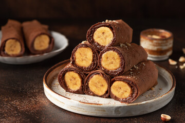 Rolled vegan chocolate crepes with banana filling on dark background. vegan thin pancakes for breakfast or dessert