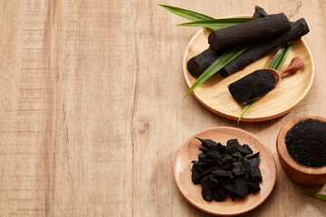 Flatlay of bamboo activated charcoal and charcoal powder decorated with green leaf in wooden...