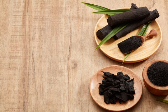 Flatlay of bamboo activated charcoal and charcoal powder decorated with green leaf in wooden background 