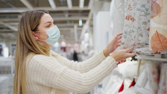 young woman in a protective mask close-up in the store chooses home textiles and bed linen