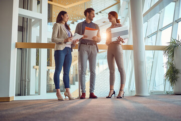 A young business man is enjoying a talk with two young female colleagues in the hallway. Business,...