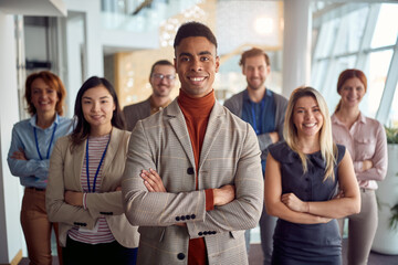 A young cheerful businessman is standing in the company building hallway with his colleagues and enjoys posing for a photo. Business, people, company