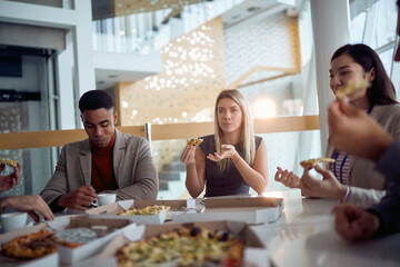 Young business people enjoy eating a pizza during a lunch break in the company building. Business,...