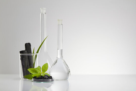 Activated charcoal research in laboratory with glassware beaker and transparent podium with green leaf and blank space in white background , front view