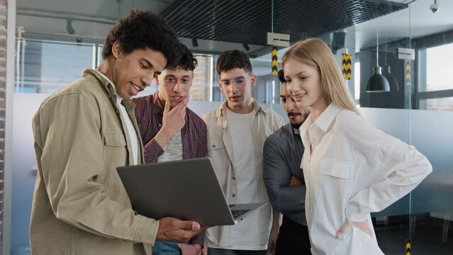Young company employee explains development strategy tells new ideas showing work plan on laptop to smiling diverse colleagues creative team discussing online project group conversation teamwork