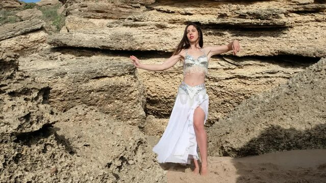 A beautiful woman performing a sensual belly dance in the sand on the beach. Spectacular landscape with blanks.