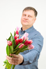 An adult male blonde holds out a bouquet of bright fragrant tulips, isolated, white background. out of focus, blurry.