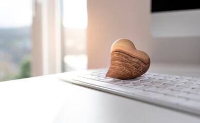 Wooden heart on keyboard in sunlight with text space. Internet dating concept.