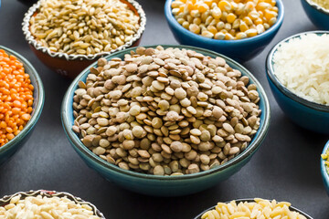 Uncooked dry cereal food group in  ceramic bowls on black surface.Selected green lentil bowl