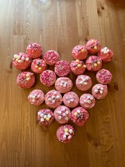 A close up view of freshly baked pink valentines day cup cakes, with pink icing and sprinkles